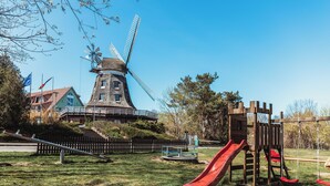 A windmill, a playground with a slide, and a building with flags. - Landhotel Lewitz Mühle (Banzkow)