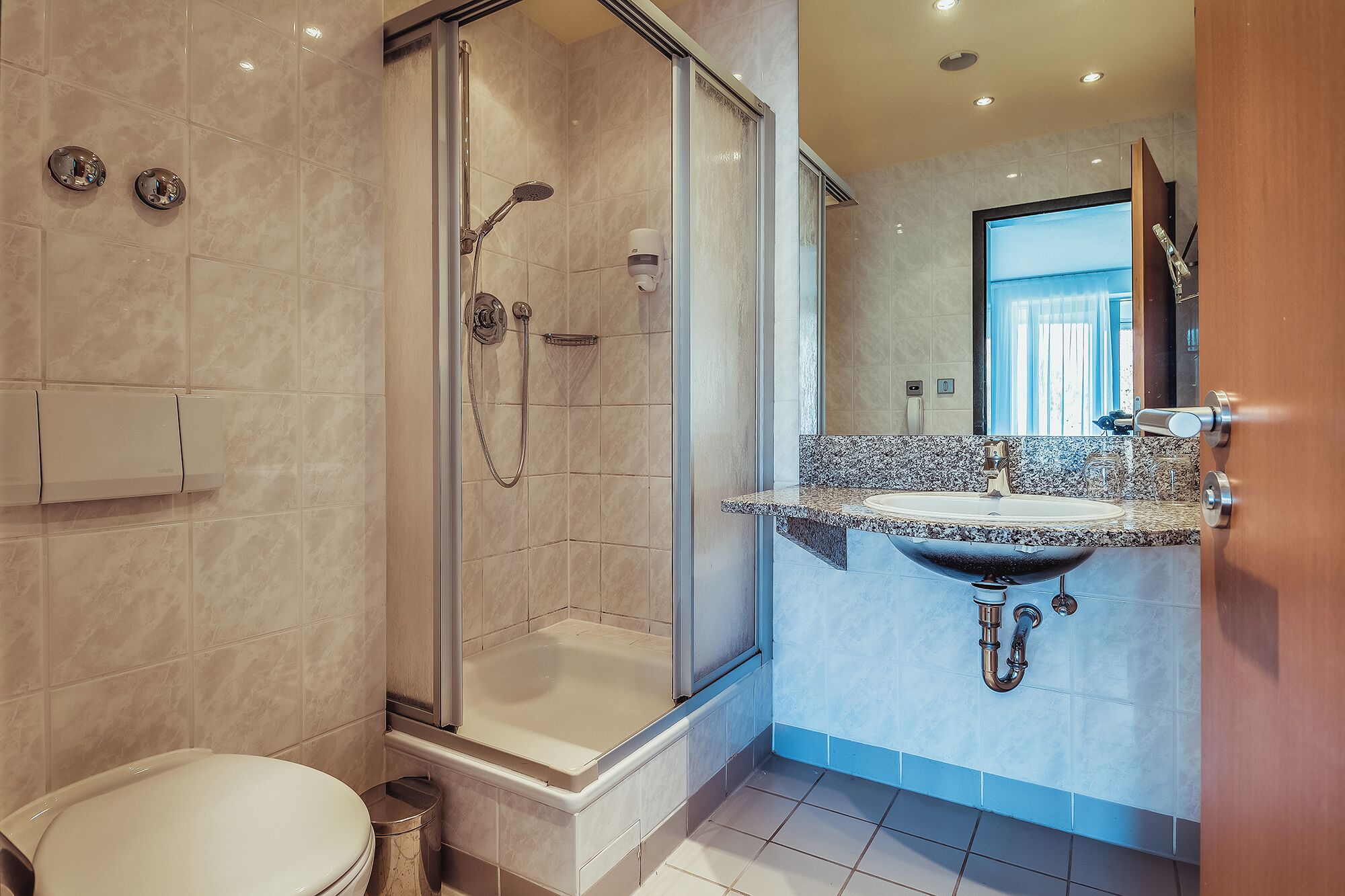 A modern bathroom with a glass-enclosed shower, a freestanding bathtub, and a granite countertop sink.
