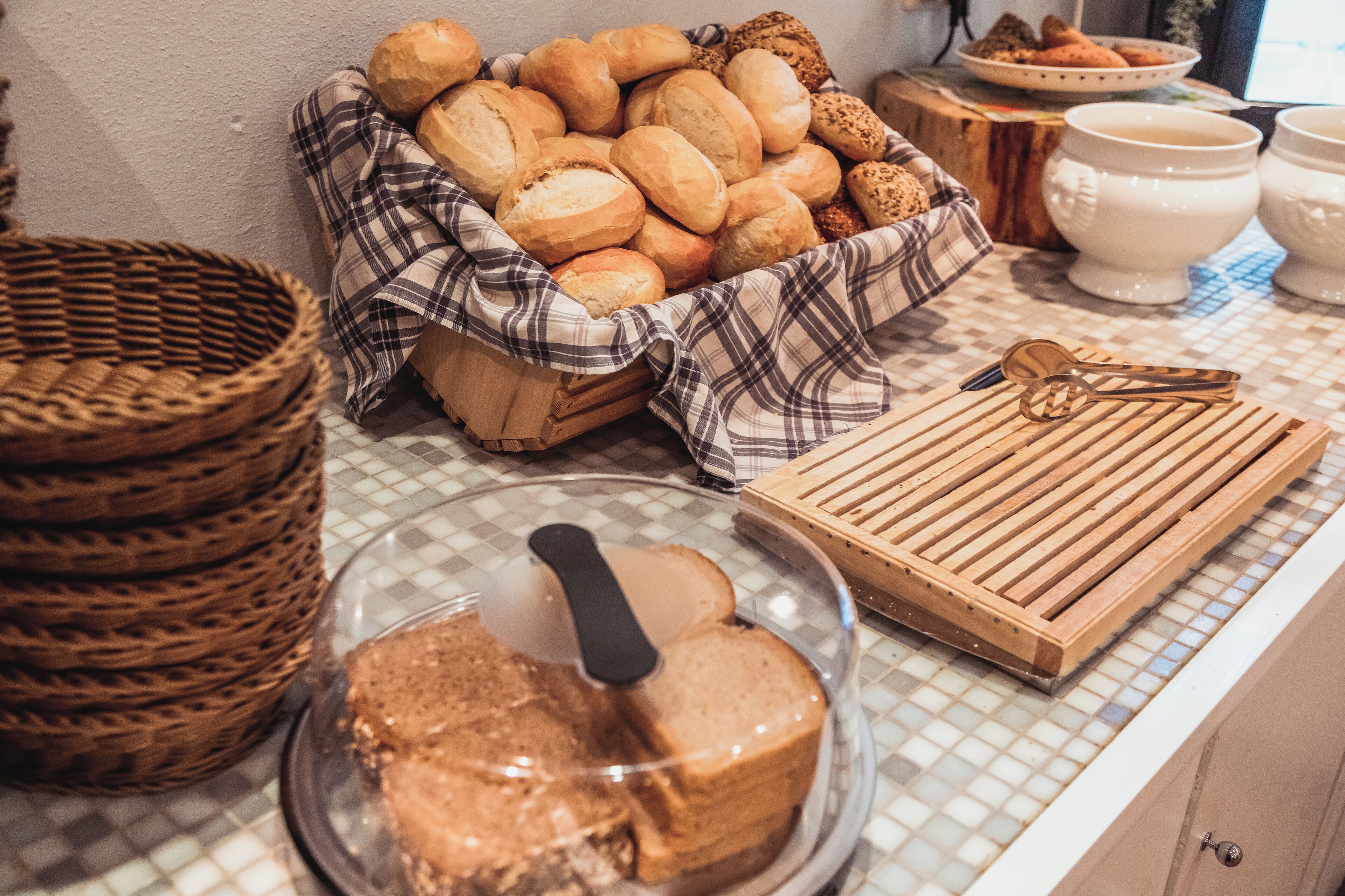 Eine Küchenarbeitsplatte mit einem Brotkorb, einem Holzschneidebrett und einem Glasbehälter mit Kuchen.