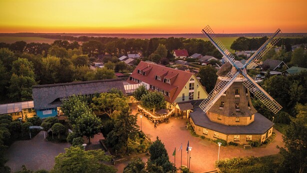 A traditional windmill surrounded by a village with a reception area and buildings with red roofs. - Landhotel Lewitz Mühle (Banzkow)