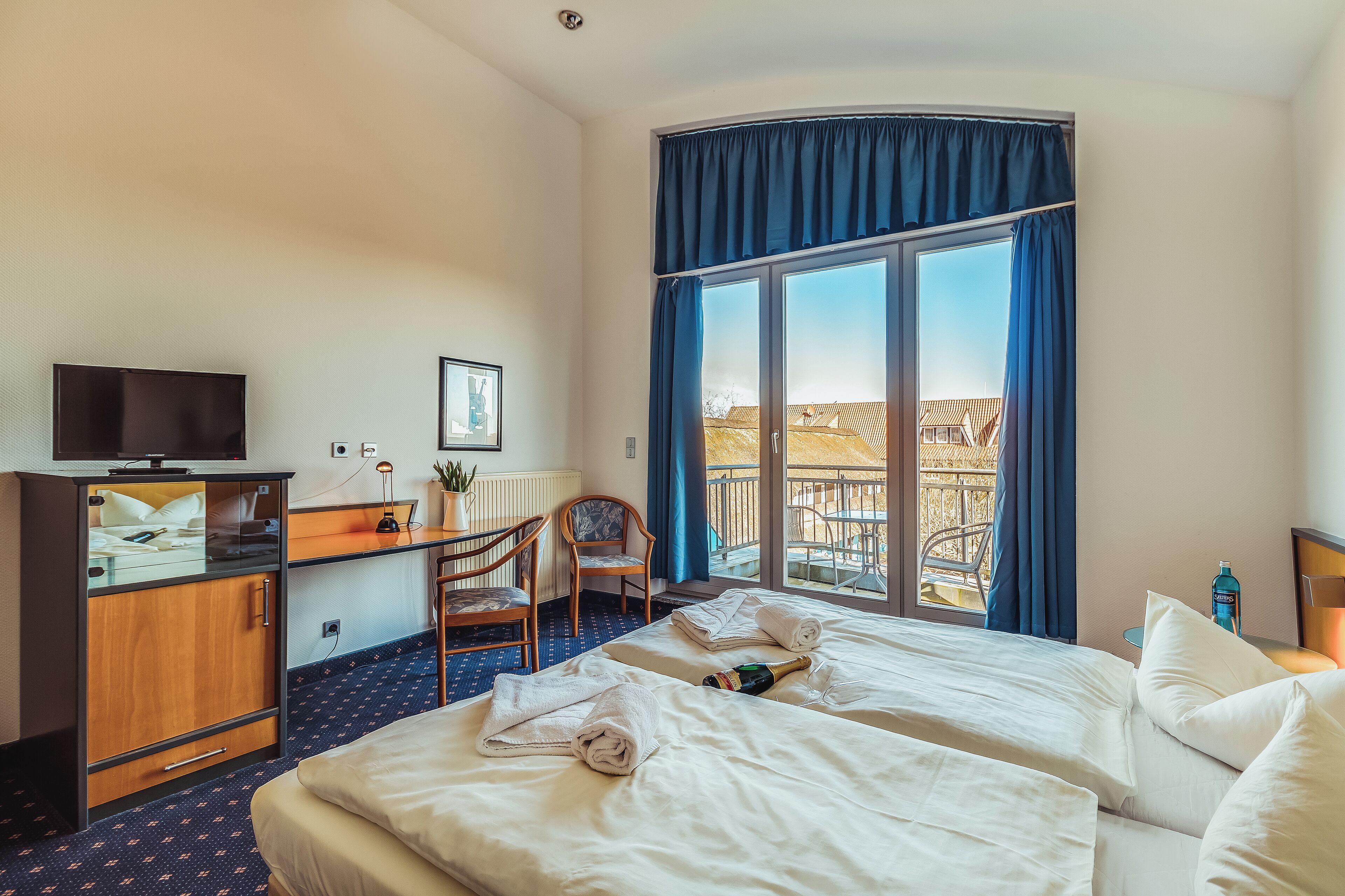 Une chambre d’hôtel avec deux lits, un bureau avec une télévision, une chaise et une grande fenêtre avec des rideaux.