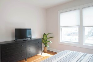 A bedroom with a bed, a dresser, a television on the dresser, a potted plant, and a window with blinds. - Adorable Broad Ripple Duplex! (Indianapolis)