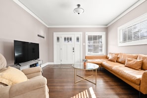 A living room with a flat-screen TV, a glass coffee table, a sofa, and a door with frosted glass panels. - Adorable Broad Ripple Duplex! (Indianapolis)