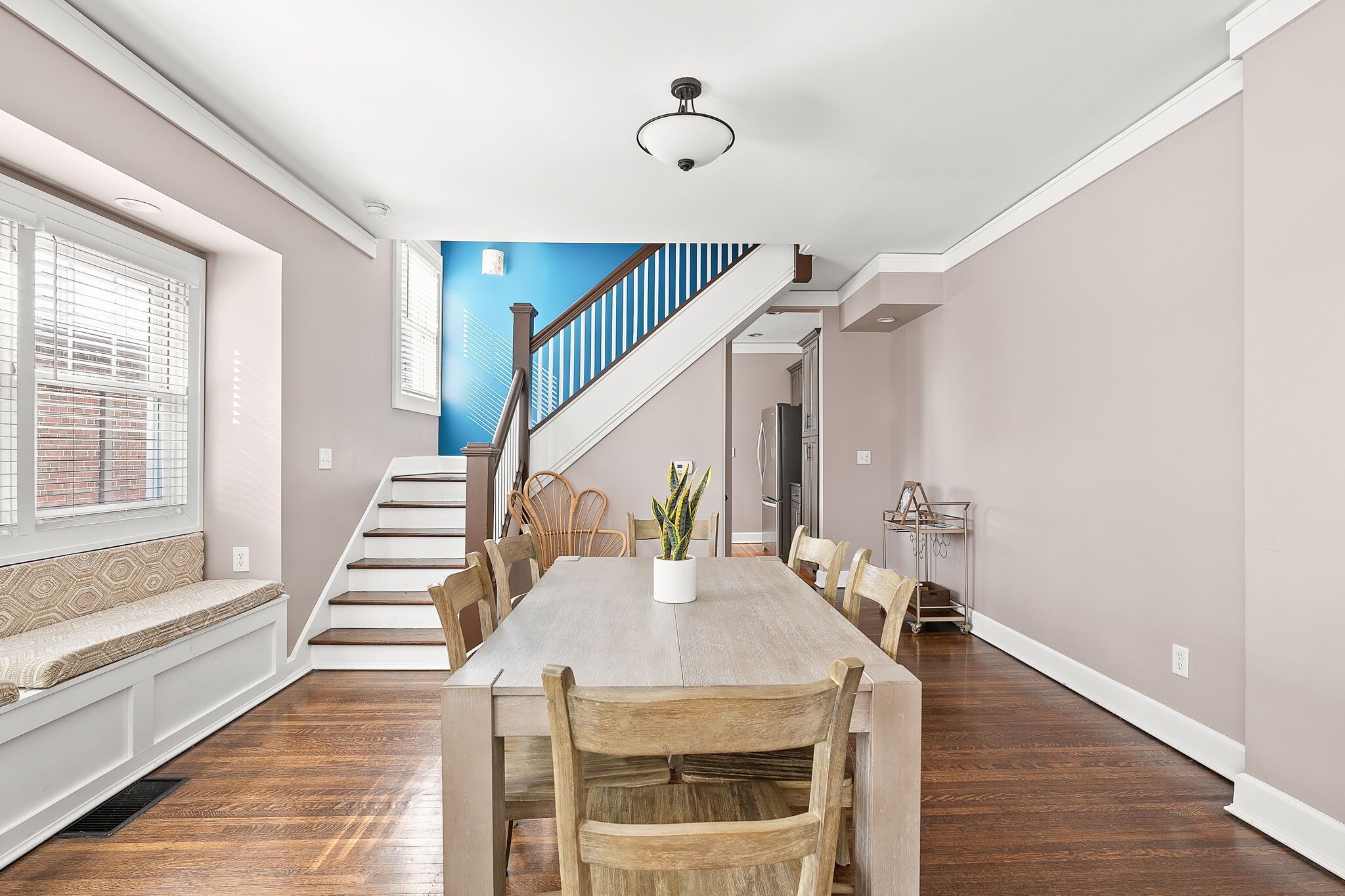 Un coin repas avec une table en bois, des chaises et un banc. Un escalier mène à une autre pièce.