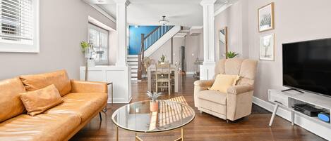 A modern living room with a leather sofa, a glass coffee table, a beige armchair, and a flat-screen TV.