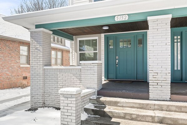 A two-story house with a teal front door, white brick columns, and a number 5152 on the overhang. - Adorable Broad Ripple Duplex! (Indianapolis)