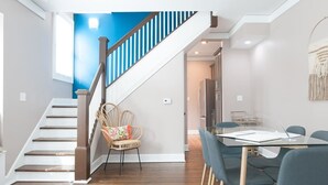 Un vaste espace de vie comprenant un escalier, une table à manger avec des chaises et, au fond, un coin cuisine.