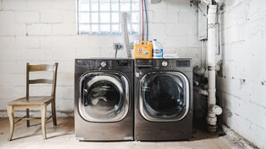 A laundry area with two front-loading washing machines, a wooden chair, and a window with a view. - Adorable Broad Ripple Duplex! (Indianapolis)