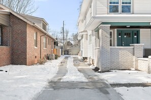A narrow, snow-covered alley between two brick houses with a concrete path.