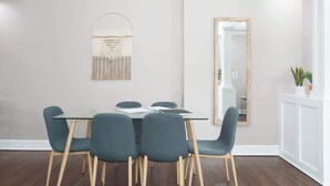 A dining area with a glass table, four chairs, a macrame wall hanging, and a mirror. - Adorable Broad Ripple Duplex! (Indianapolis)