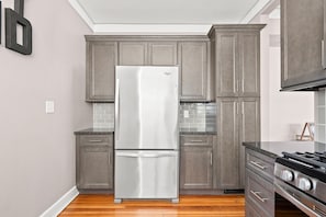A kitchen with grey cabinets, a stainless steel refrigerator, a tiled backsplash, and a gas stove. - Adorable Broad Ripple Duplex! (Indianapolis)