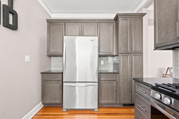 A kitchen with grey cabinets, a stainless steel refrigerator, a tiled backsplash, and a gas stove.