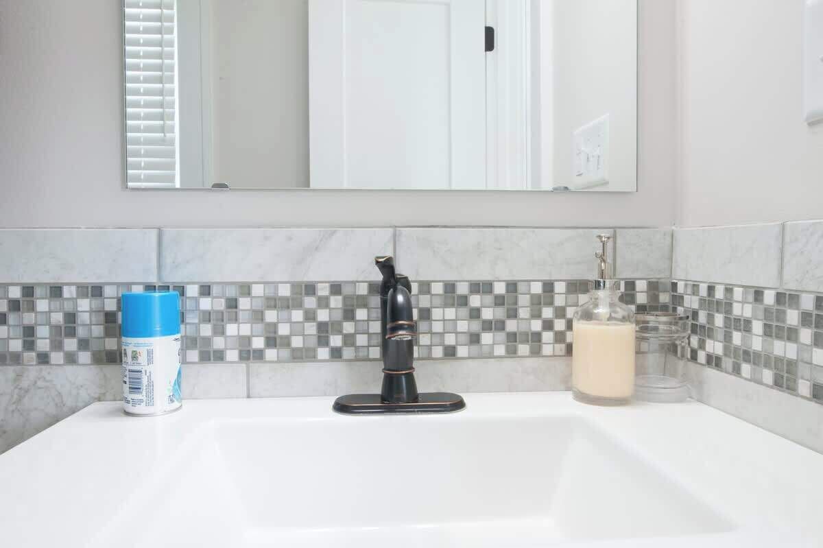 Ein Badezimmer mit einer weißen Spüle, einem schwarzen Wasserhahn, einer blauen Flasche und einer Glasflasche mit weißer Flüssigkeit.