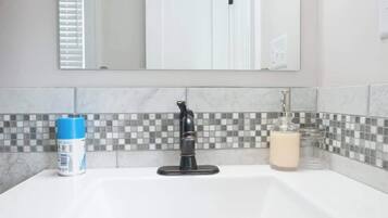 Ein Badezimmer mit einer weißen Spüle, einem schwarzen Wasserhahn, einer blauen Flasche und einer Glasflasche mit weißer Flüssigkeit.