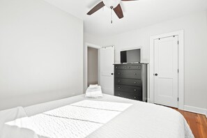 A bedroom with a bed, a dresser, a television, and two doors.