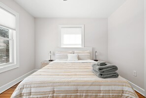 A bedroom with a large bed, a window, and a nightstand with a lamp.