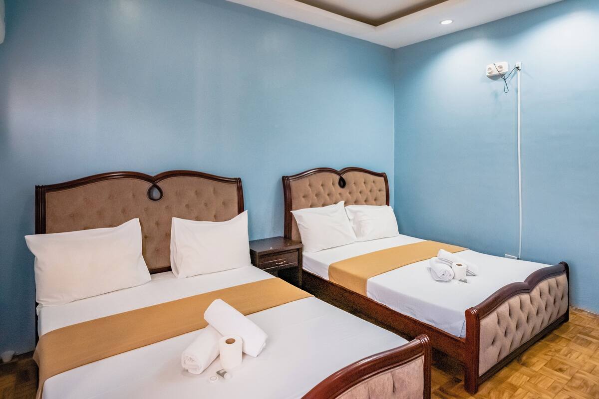 A hotel room with two beds, wooden headboards, beige bedsheets, and a wooden floor.