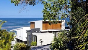 A modern house with a view of the ocean, surrounded by lush greenery. - Coolum Bays Beach House - Discover ultimate luxury at this award-winning architectural masterpiece. (Coolum Beach)