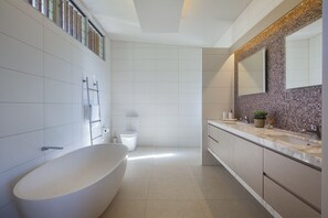 Un baño moderno con una bañera independiente, un inodoro y un lavamanos con un respaldo de mosaicos.