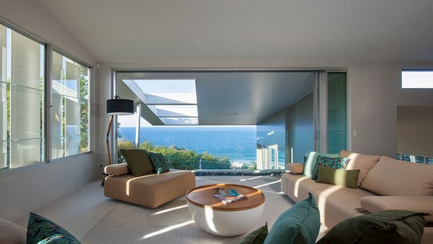 A modern living room with large windows, a round coffee table, and two sofas with cushions. - Coolum Bays Beach House - Discover ultimate luxury at this award-winning architectural masterpiece. (Coolum Beach)