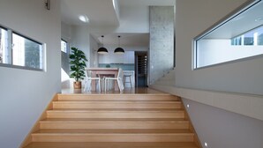 A modern interior with a wooden staircase leading to a dining area with white chairs and a table. - Coolum Bays Beach House - Discover ultimate luxury at this award-winning architectural masterpiece. (Coolum Beach)