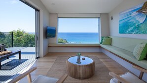 A modern living room with a large window overlooking the ocean, a round coffee table, and a green sofa. - Coolum Bays Beach House - Discover ultimate luxury at this award-winning architectural masterpiece. (Coolum Beach)
