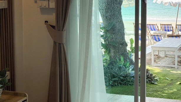 Habitació d'hotel amb un llit, una finestra amb cortines i vista a la platja, i una tovallola sobre el llit.
