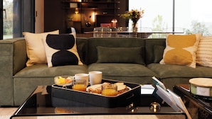 Una sala moderna con un sofá modular, una mesa de centro de vidrio y una bandeja con alimentos para el desayuno.