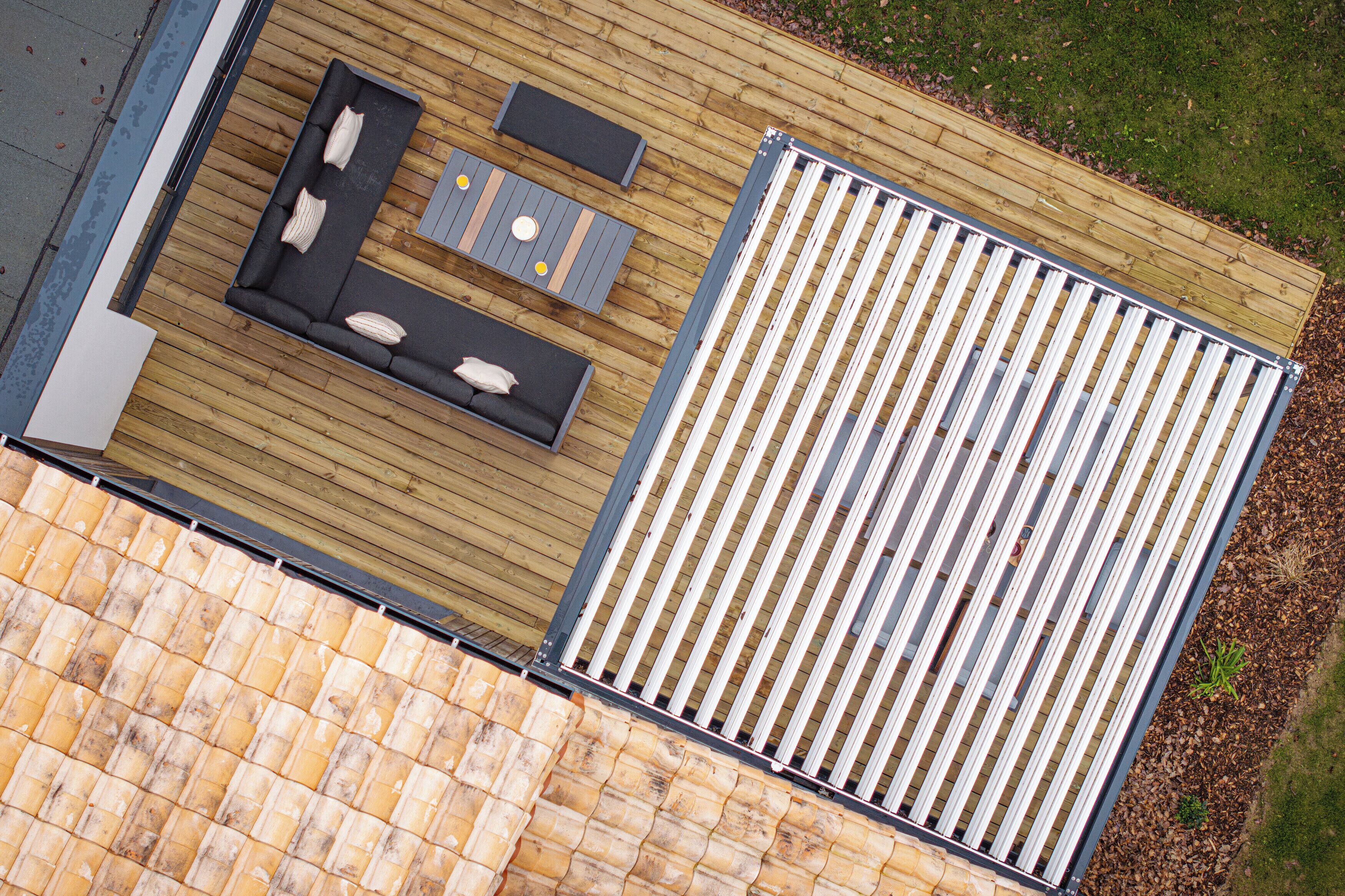 Une terrasse sur le toit, dotée d’un plancher en bois, d’une rambarde en métal et d’un espace détente avec des coussins et une table.