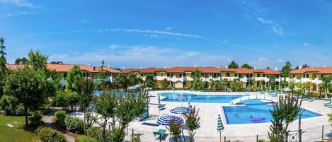A hotel with multiple swimming pools, a landscaped garden, and a row of yellow buildings with red roofs.