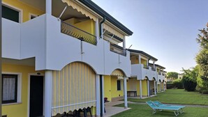 A multi-story hotel with balconies, a covered outdoor seating area, and a well-maintained lawn. - Relaxing getaway with pool and garden in Bibione (San Michele Al Tagliamento)