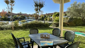 An outdoor seating area with a table and chairs, a sign reading "BEACH," and a pool in the background. - Relaxing getaway with pool and garden in Bibione (San Michele Al Tagliamento)