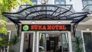 The entrance of Suka Hotel with a glass facade, a signboard, and potted plants. - Suka Hotel (Tan Ninh)