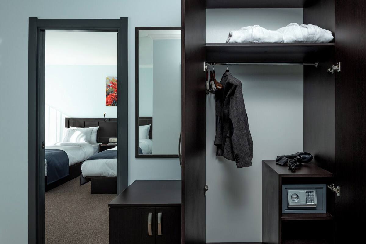 A hotel room with a bed, a wardrobe with a mirror, a coat rack, and a safe.