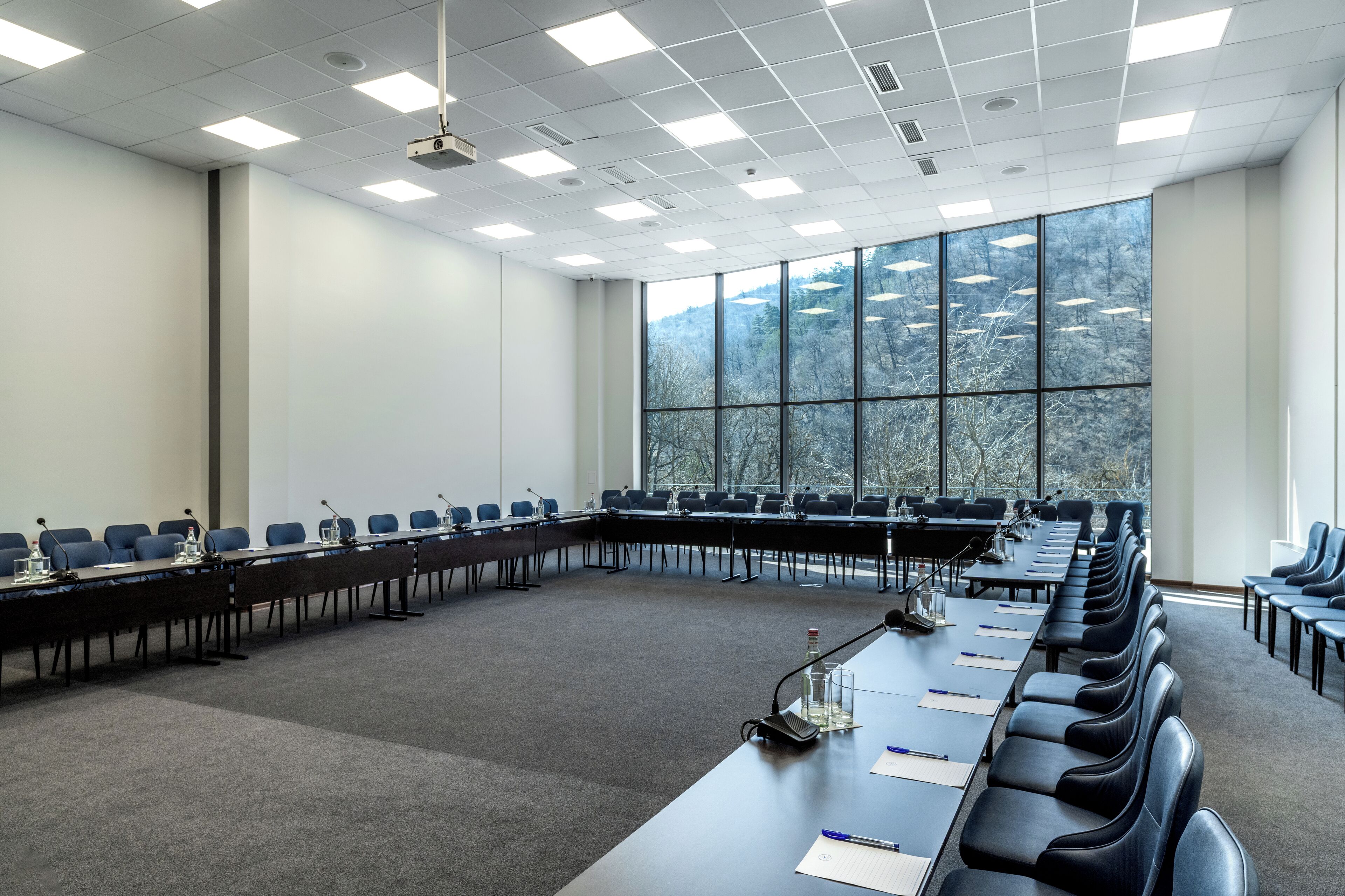 Een vergaderzaal met een lange tafel, stoelen en een groot raam met uitzicht op bomen.