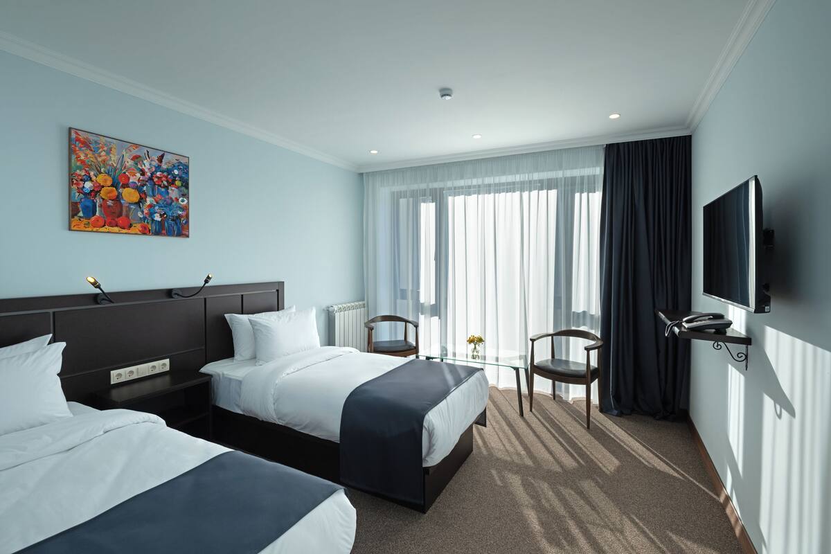 A hotel room with two beds, a television, a painting, and a view of the outdoors.