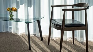 Una habitación moderna con una mesa de vidrio, una silla de madera y cortinas translúcidas.