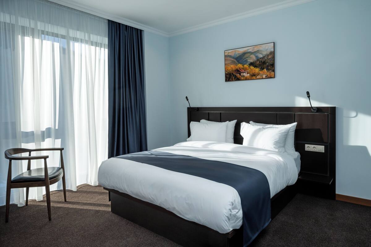 A hotel room with a large bed, a chair, a desk, and a painting on the wall.