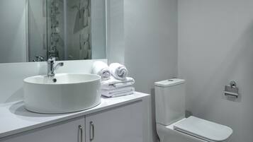 Een moderne badkamer met een witte wastafel, een grote spiegel, een toilet en een handdoekhouder.