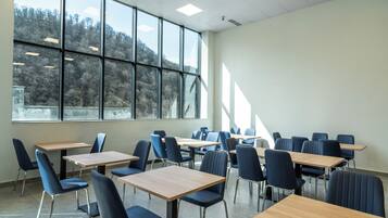 A classroom with multiple desks and chairs, large windows, and a view of trees outside.
