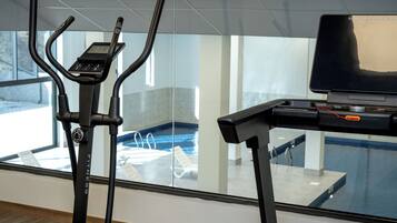 Una máquina de ejercicio y un portátil sobre un escritorio, con vista a una piscina.