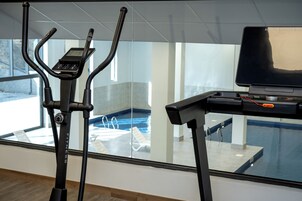 Una máquina de ejercicio y un portátil sobre un escritorio, con vista a una piscina.
