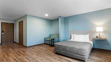 Una habitación de hotel con una cama, una silla, una mesita, una lámpara y una puerta.