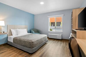 Ein Hotelzimmer mit Bett, Schreibtisch, Fernseher, Fenster und Wandheizung.