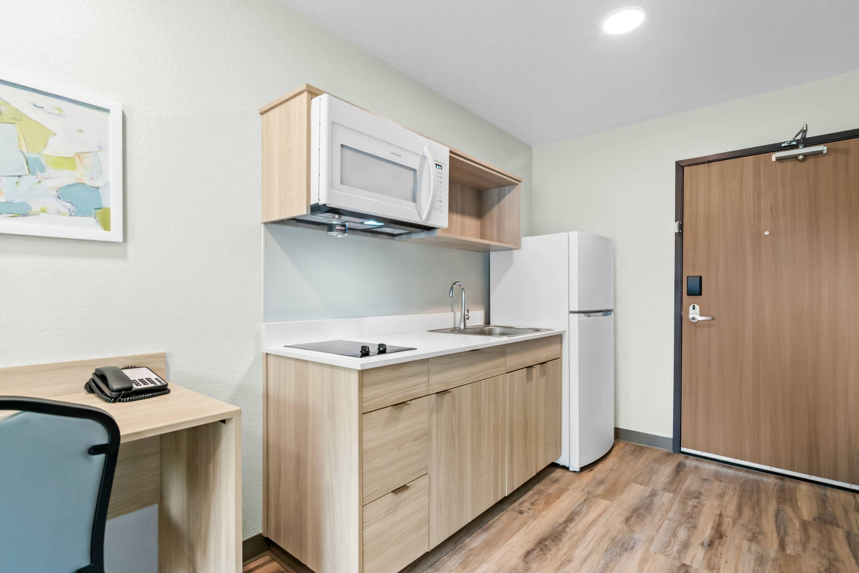 A compact kitchen with a microwave, sink, and refrigerator, wooden cabinets, and a map on the wall.