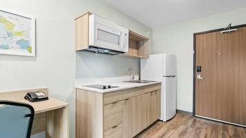 A compact kitchen with a microwave, sink, and refrigerator, wooden cabinets, and a map on the wall.