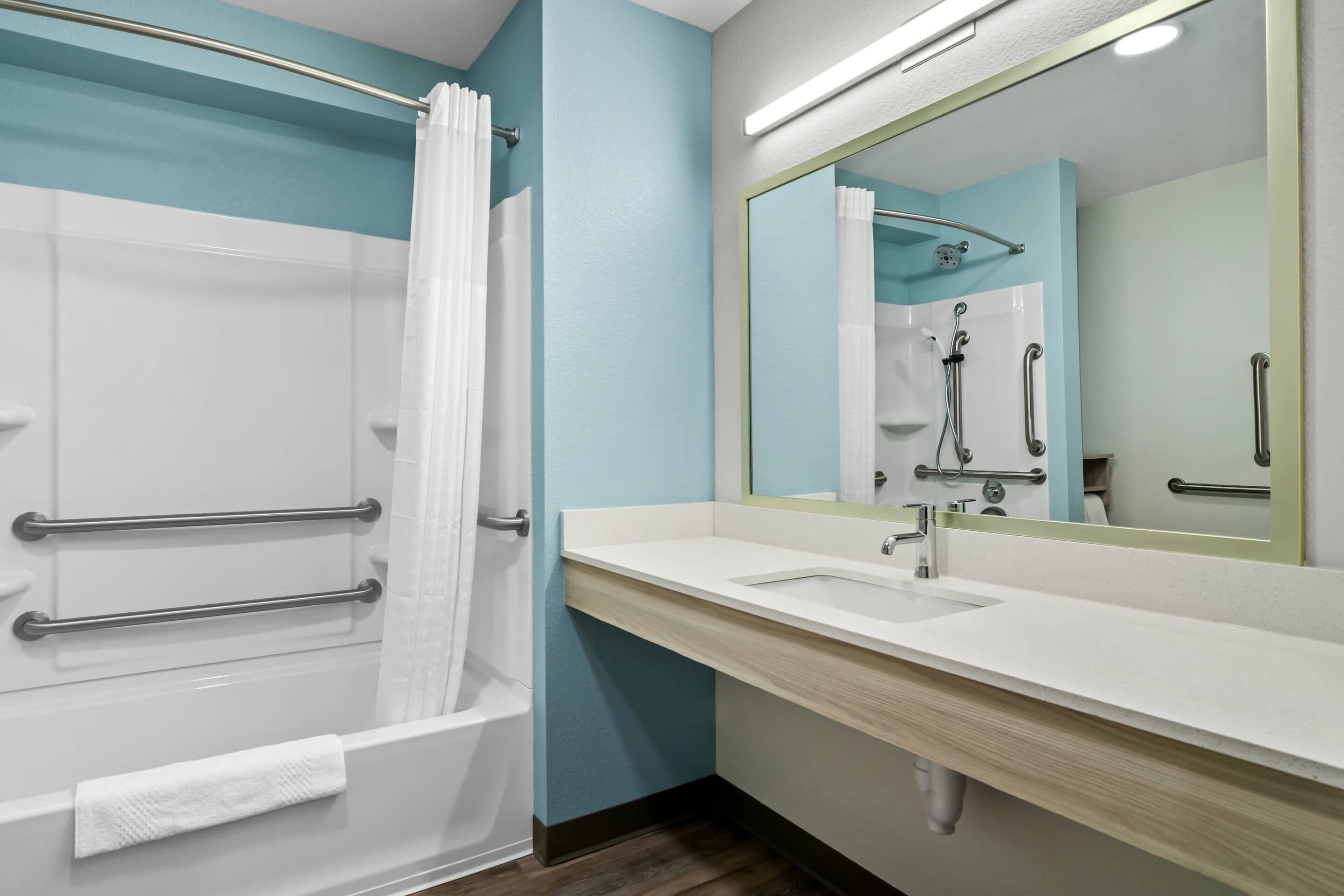 A bathroom with a bathtub, a sink, a mirror, and a shower with grab bars.
