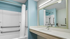 Une salle de bain équipée d’une baignoire, d’un lavabo, d’un miroir et d’une douche avec des barres d’appui.