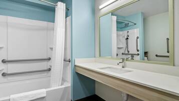 A bathroom with a bathtub, a sink, a mirror, and a shower with grab bars.