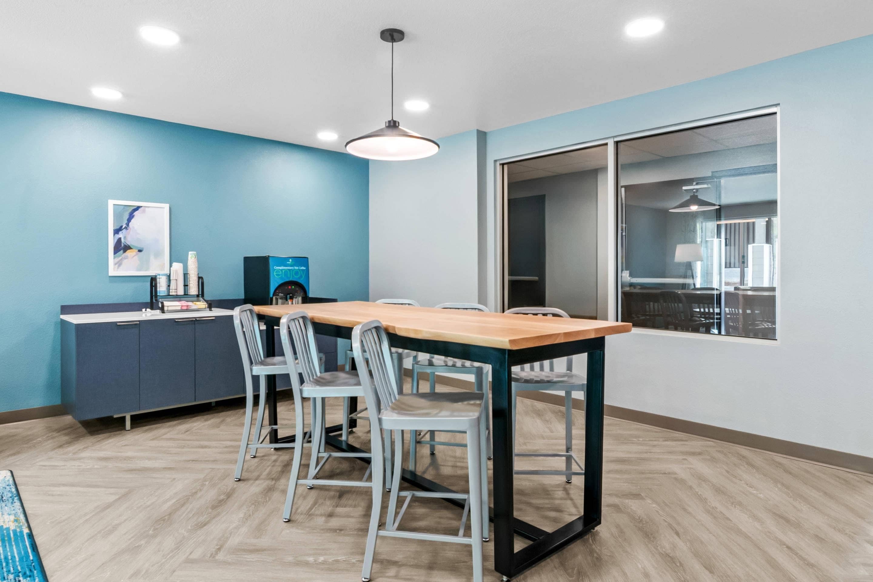 A conference room with a long table, four chairs, a cabinet with items, and a window with a view.
